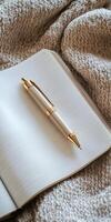A stylish gold pen rests on an open notebook, surrounded by a cozy textured blanket, capturing a warm and inviting atmosphere. photo
