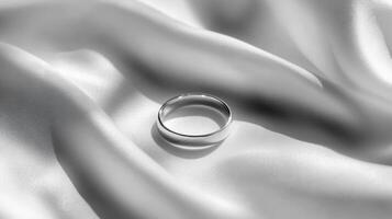 A sleek silver ring resting on smooth white silk, showcasing elegance and luxury in a minimalist style. photo