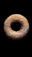 A delectable glazed doughnut lightly dusted with powdered sugar against a stark black background, showcasing its inviting texture and sweet appeal. Perfect for dessert lovers. photo