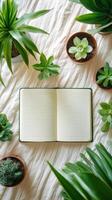 Open notebook with lined pages surrounded by green succulents on a white fabric surface, perfect for creative inspiration. photo