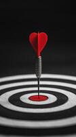 A red arrow is standing on a black and white target. The arrow is pointing towards the center of the target, which is also black and white. The target is circular in shape photo