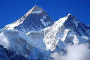 Two snow covered mountains with a blue sky in the background. The mountains are covered in snow and appear to be very tall photo