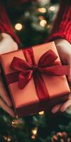de cerca de manos presentación un rojo regalo caja con un reluciente cinta, conjunto en contra un fondo de brillante Navidad árbol luces. foto