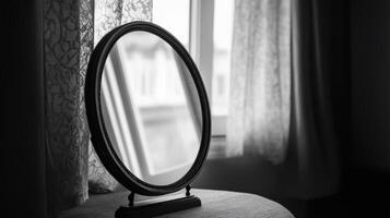 A vintage mirror on a table with lace curtains, capturing soft natural light in a black and white setting. photo