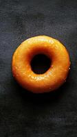 This image showcases a delicious glazed donut with a shiny surface, set against a dark background. Perfect for food-related projects or dessert menus. photo