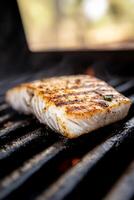Piece of fish is being grilled on a grill. The fish is brown and has a lot of seasoning on it photo