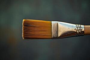 A paintbrush with a wooden handle and a silver tip. The bristles are brown. The brush is laying on a table photo