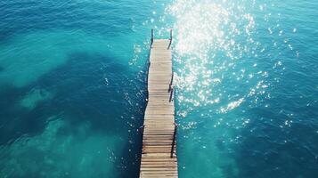 Stunning aerial shot of a wooden pier stretching into a vibrant turquoise sea, with sunlight creating a sparkling effect on the water. photo