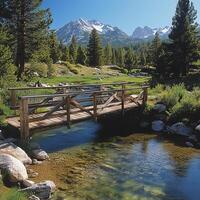 A picturesque view of a wooden bridge crossing a clear stream in a lush valley with majestic mountains in the background. photo