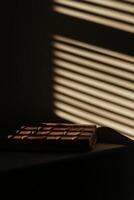 A captivating image of a brown chocolate bar resting on a table, illuminated by soft sunlight filtering through blinds, creating beautiful shadows and patterns. photo