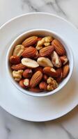 Bowl of nuts is on a white plate. The nuts include almonds, walnuts, and cashews photo