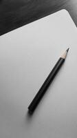 A black pencil resting on a blank white sheet, showcasing minimalist design and creative potential in a monochrome setting. photo