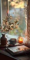 A vase with flowers sits on a table next to a book and a cup of coffee photo