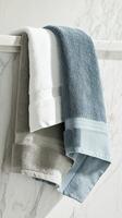 Three soft cotton towels in gray, blue, and white hang stylishly on a marble surface, enhancing the modern bathroom's elegant design and inviting comfort. photo