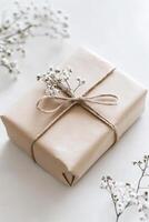 Brown box with white flowers tied to it is placed on a white surface. The flowers are small and white photo