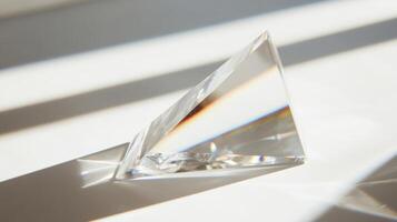 A clear crystal object is sitting on a white surface. It is a triangle shape. The light is shining on it, creating a beautiful reflection photo