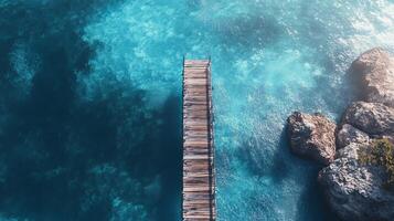 Stunning aerial shot of a wooden pier reaching into vibrant turquoise waters, surrounded by rocky coastline and sunlit ocean. photo