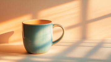 A blue coffee cup is sitting on a table. The cup is in the sun and the shadow of the cup is on the table photo
