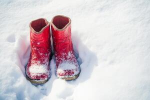 Two red boots are sitting in the snow. The boots are made of rubber and are bright red in color photo
