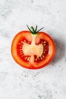 Close-up of a fresh half tomato on a light textured surface, highlighting its vibrant red color and juicy interior. photo