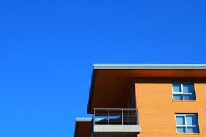 Low-angle view of a modern brick building with a balcony and windows set against a clear blue sky, showcasing minimalist architecture. photo