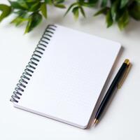 A spiral bound notebook sits on a table with a pen next to it. The notebook is empty, and the pen is black photo