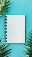 Open blank spiral notebook surrounded by green palm leaves on a turquoise background, perfect for creative projects and planning. photo
