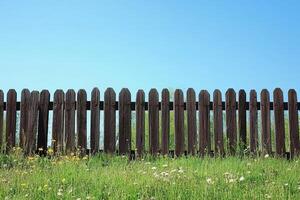 Rustic Wooden Fence with Wildflowers Under Clear Blue Sky in a Serene Countryside Setting photo