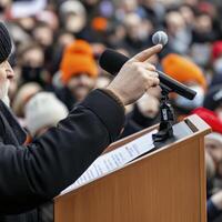 Man Giving Speech at Podium to Crowd Outdoors photo