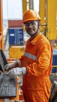 Male Worker in Orange Jumpsuit Operating Computer at Industrial Site photo