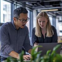 Two Colleagues Collaborating on a Laptop in a Modern Office Setting, Discussing Business Strategies and Analyzing Data, Focused on Achieving Project Goals with Teamwork and Communication, Utilizing photo