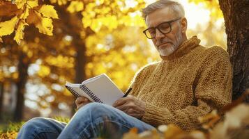 Captivating Autumn Portrait A thoughtful middle-aged man with glasses, immersed in reading his journal under a vibrant yellow maple tree, bathed in the warm glow of the setting sun The crisp air of photo