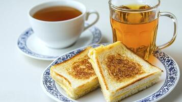 Indulge in a serene tea break with this inviting still life featuring golden grilled cheese sandwiches, steeped tea in a delicate white cup and clear mug, all arranged on a blue and white patterned photo