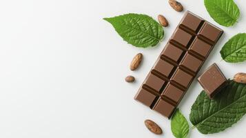 Indulge in the rich allure of chocolate This captivating image showcases a delectable bar of milk chocolate alongside fresh green leaves and cocoa beans, evoking feelings of sweetness, natural photo