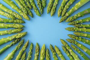 Fresh green asparagus spears arranged in a circular pattern on a vibrant light blue background, creating a visually appealing and healthy food concept ideal for culinary blogs, recipe websites, or photo