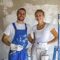 A joyous couple stands proudly before a freshly painted wall, splattered with vibrant colors, their smiles radiating pure happiness Their collaborative effort is evident in the streaks of paint on photo
