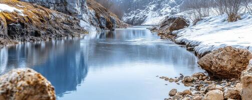 A serene landscape unveils a crystal-clear river, its surface mirroring the soft winter sky above The riverbed, adorned with sand and pebbles, is visible through the transparent water Snowy banks photo