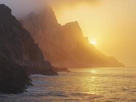 As the sun ascends, its golden embrace gently kisses the fog-laden cliffs, creating a breathtaking spectacle The soft light dances upon the misty veil, unveiling the rugged beauty of the landscape photo