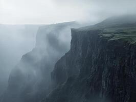 Enshrouded in mystery, a colossal canyon unveils its majestic steep walls, sculpted by the relentless hand of erosion over eons The dense fog adds an ethereal quality, blurring the lines between photo