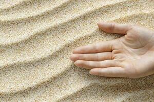 In a moment of serene connection, a woman's hand delicately traces ephemeral patterns upon the soft, yielding sand This gentle dance between skin and earth evokes feelings of mindfulness and photo