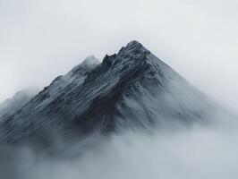 In a realm where mist dances with stone, behold the ethereal embrace of fog-veiled mountains Jagged peaks emerge like ancient sentinels, their rugged forms softened by the delicate touch of swirling photo