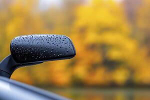 A closeup of the rearview mirror on an autumn day, with raindrops visible and trees on blur background photo