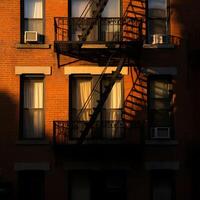Warm sunlight on brick building with metal fire escape creating sharp urban shadows on facade photo