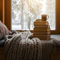 Stack of books with knitted blanket and coffee mug on window sill overlooking snowy forest winter cozy scene photo