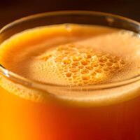 Close up of a foamy orange juice in transparent glass with soft bokeh background and fresh citrus tones photo