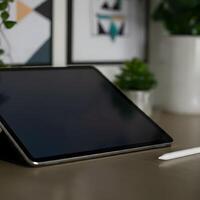 Digital tablet with blank screen on a wooden desk with white stylus and potted green plants in modern home office photo