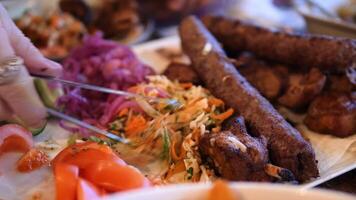 Lula kebab, a popular middle eastern dish of grilled minced meat, served with a colorful salad of chopped tomatoes, cucumbers, and pickled red cabbage, being arranged on a plate by a chef video