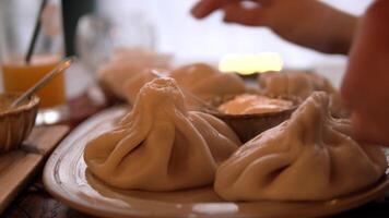 Chef demonstrates the traditional way to enjoy khinkali, carefully holding the dumpling by its top knot to prevent the flavorful broth from spilling video