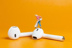 Tiny figurine of a woman appears to clean an oversized earbud photo