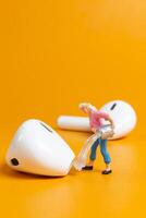 A tiny figurine of a woman appears to clean an oversized earbud on yellow background photo